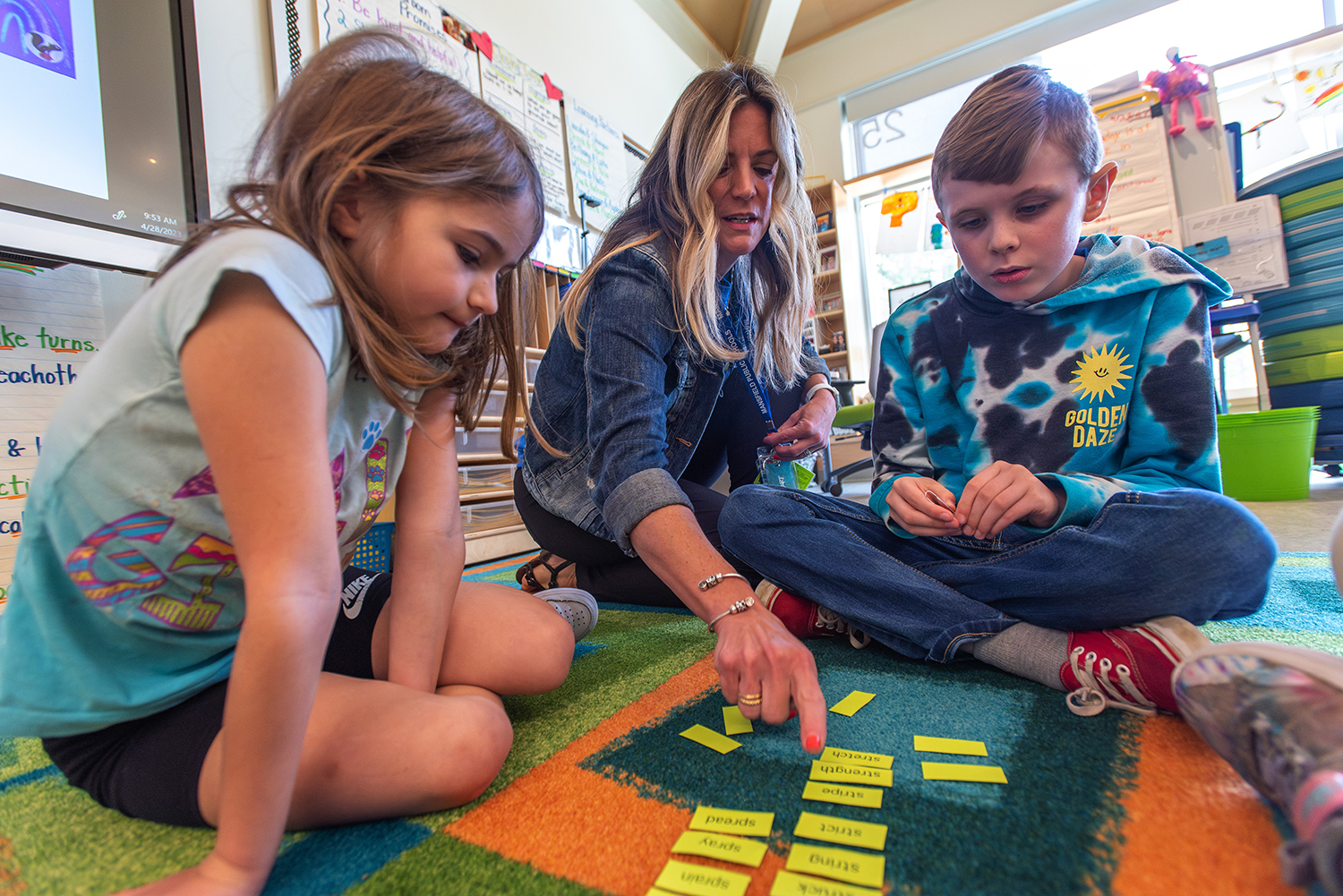 Female educator works with young students on the floor in a classroom.