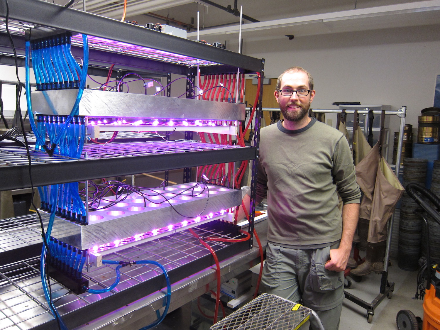 a person stands in a lab next to a metal shelf with growing lights attached.