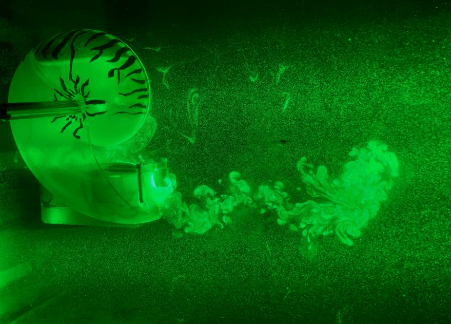 Green-illuminated image showing a nautilus-shaped robotic device expelling fluid in swirling patterns, visualizing underwater jet propulsion.