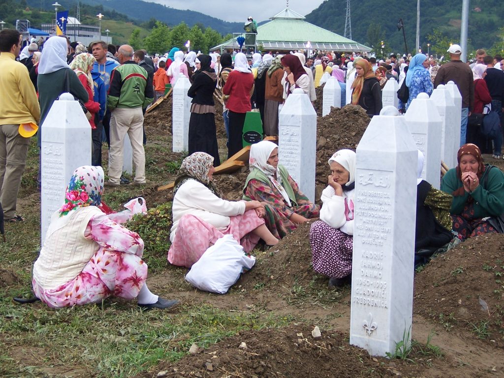 Srebrenica Memorial Cemetery at the 12th anniversary of the massacre, July 11, 2007. Women are sitting on the ground in front of the gravestones. There are crowds of people in the background.