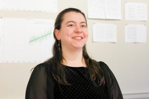 Woman with dark hair stands in front of a board with papers pinned on it