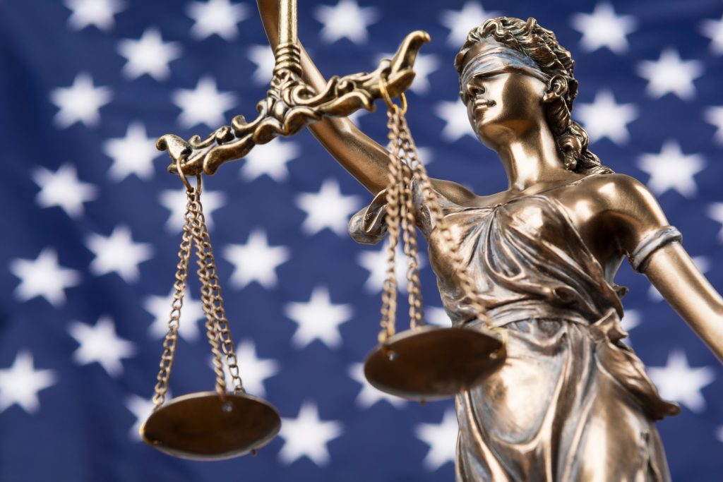 The statue of justice Themis or Justitia, the blindfolded goddess of justice against a flag of the United States of America.