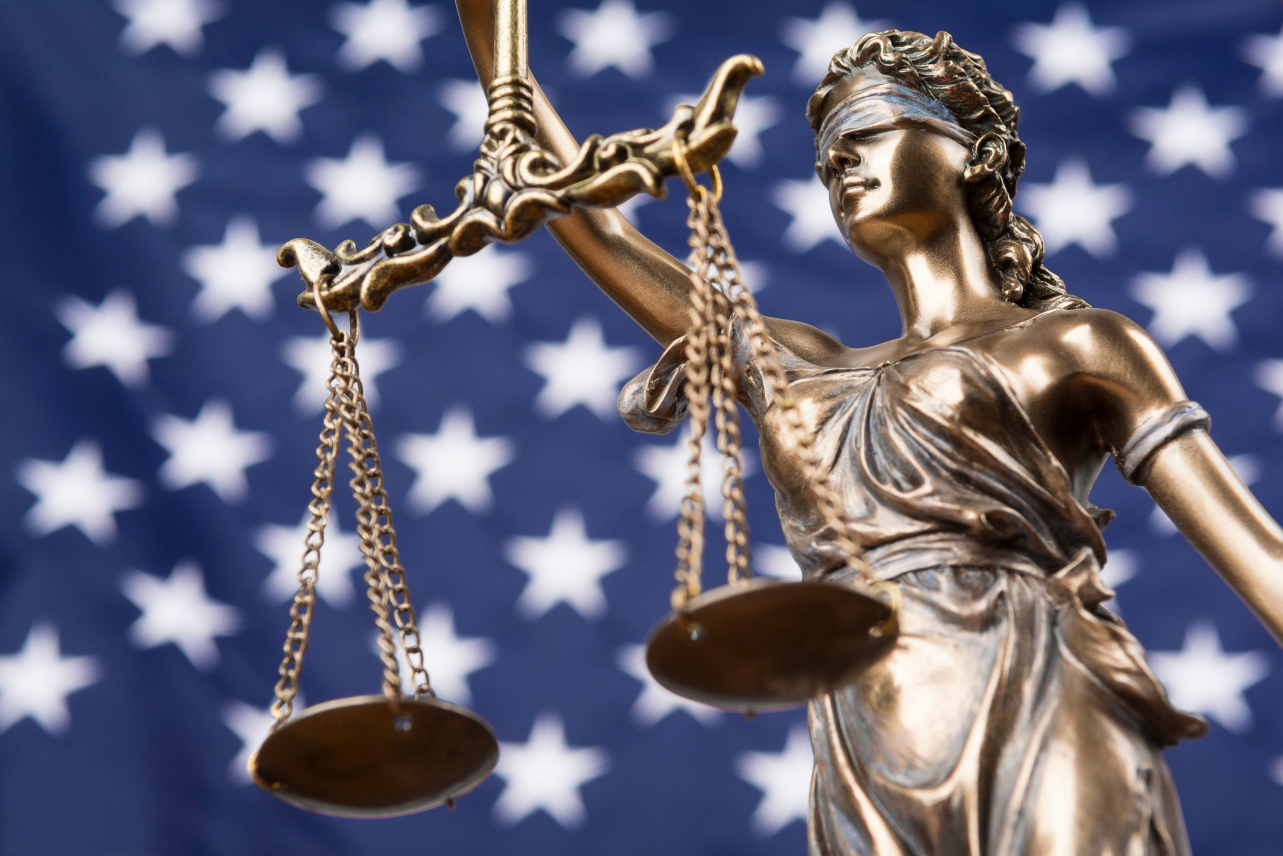 The statue of justice Themis or Justitia, the blindfolded goddess of justice against a flag of the United States of America.