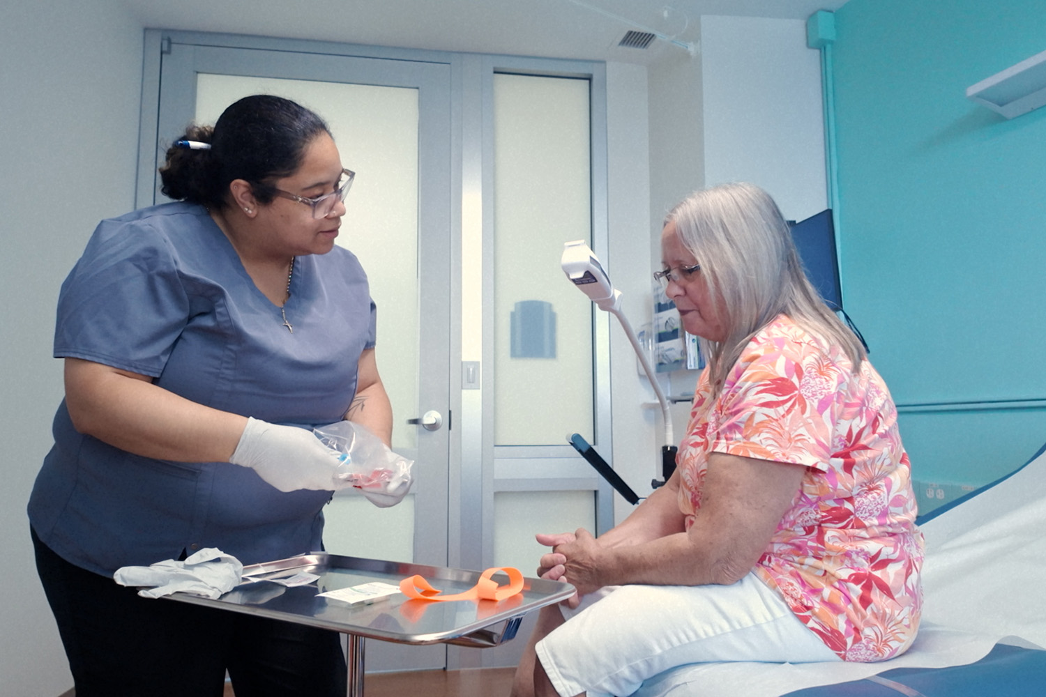 An older woman sits in the doctor's office while a nurse preps her to get blood drawn