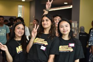 Three female students and one male student posing in black t-shirts holding up peace signs