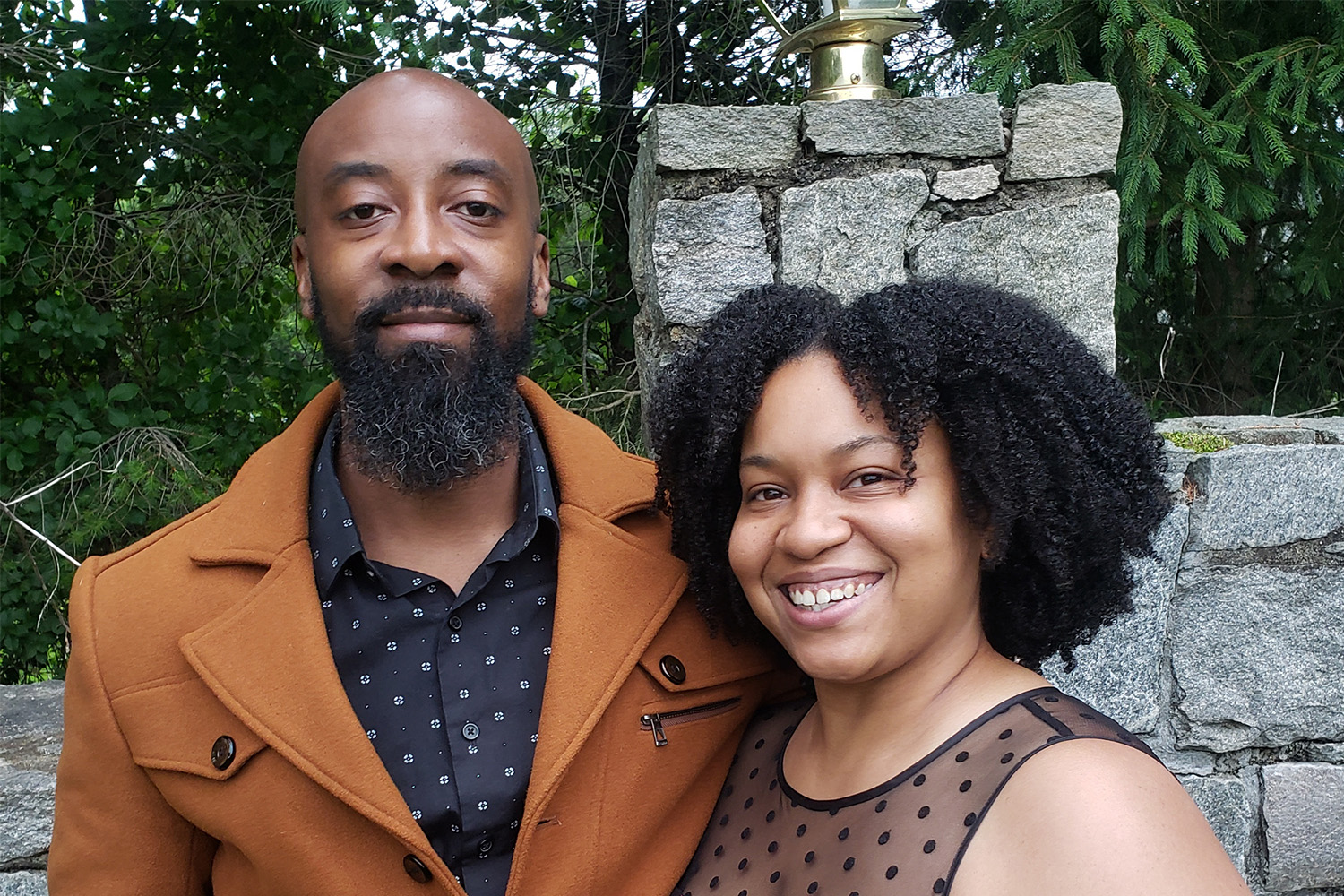 A male and a female posing for a photo in front of a stone wall