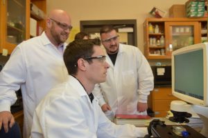 Three guys in white lab coats looking at a computer