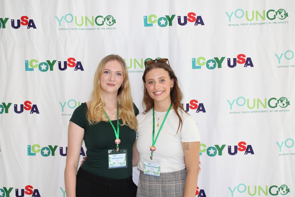 Two women posing for a photo in front of a backdrop that says LCOY USA