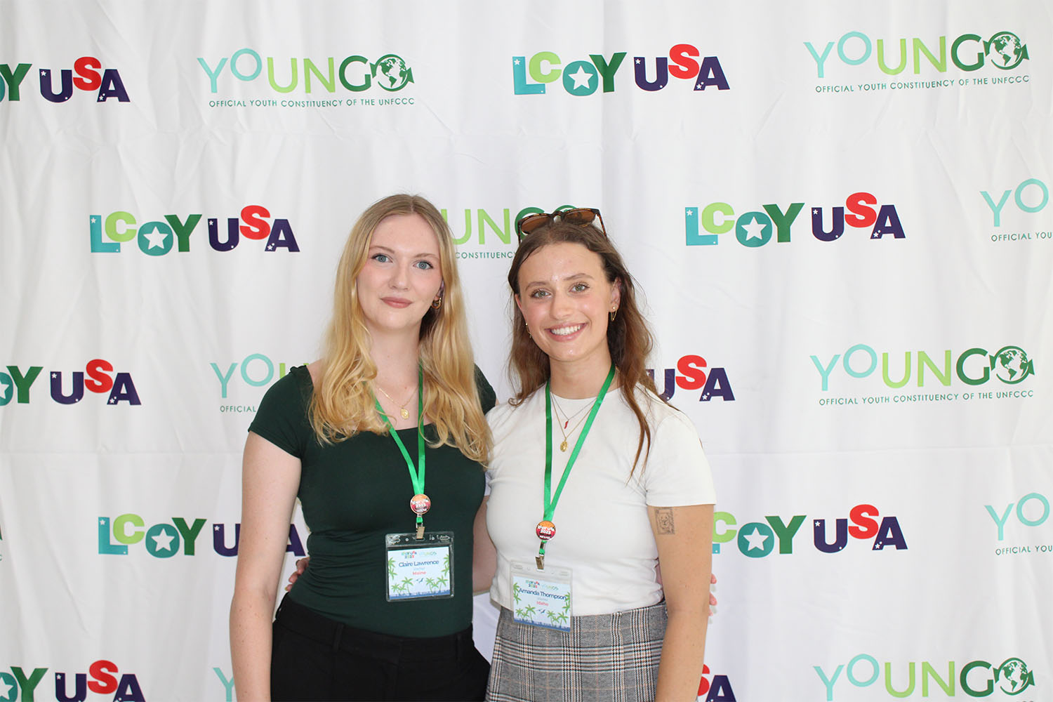 Two women posing for a photo in front of a backdrop that says LCOY USA