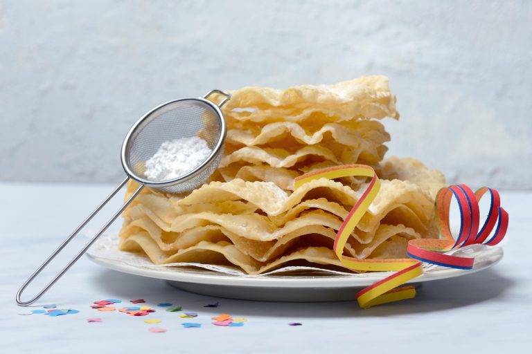 Deep-fried Fasnachtsgebaeck stacked with powdered sugar in a sifter on top and confetti on the table