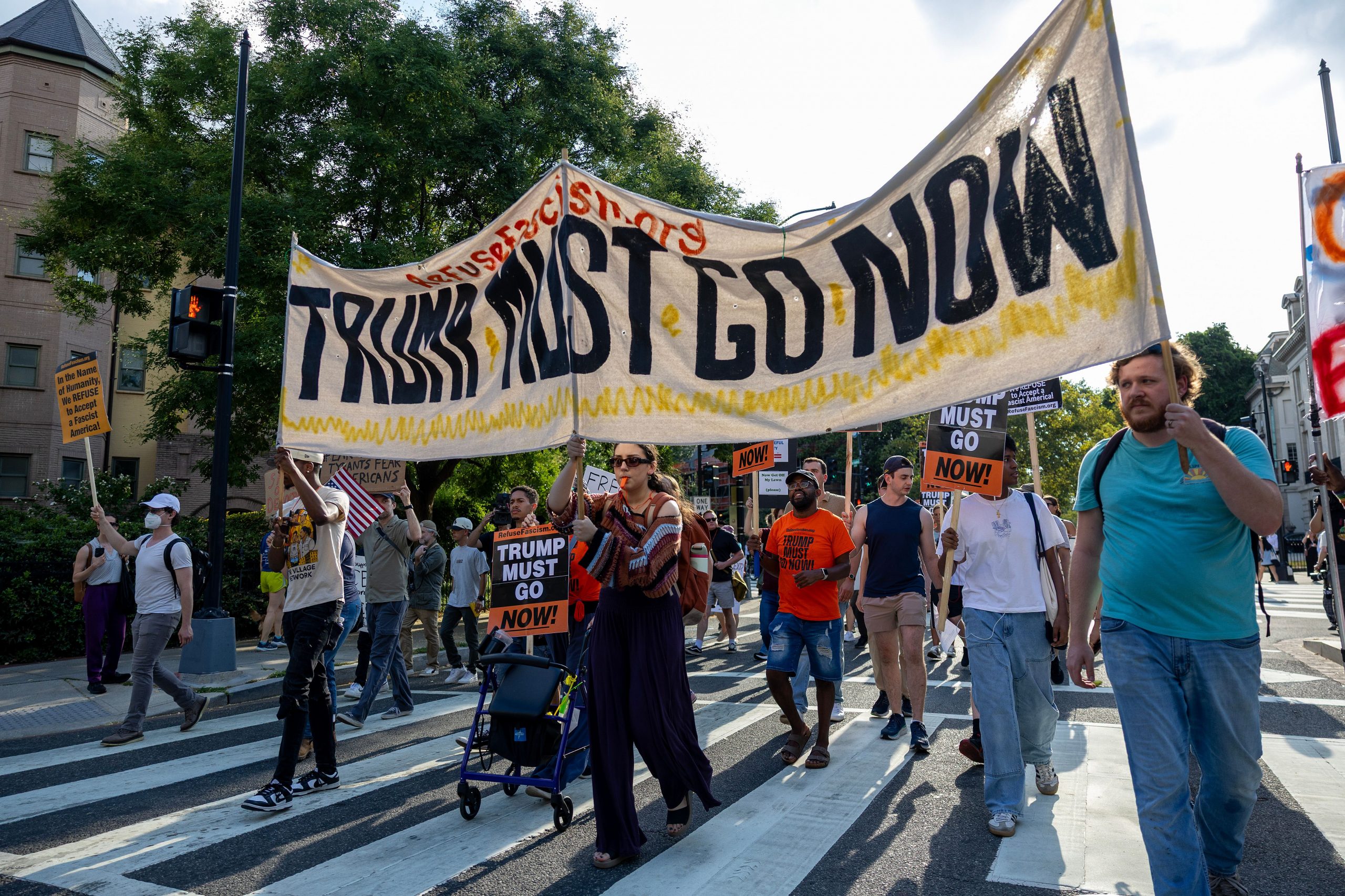 Protesters march in Washington, DC with a banner that read "Trump Must Go."