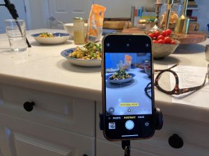 The image of a bowl of salad sitting on a kitchen counter is reflected through the view finder of a cellphone camera.
