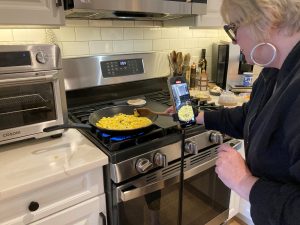 A woman stirs a pan of corn on the stovetop.