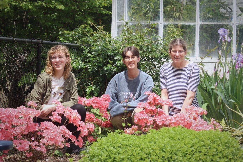 Two students and a professor smile outside a greenhouse