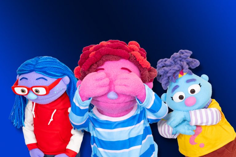 Three colorful puppet characters stand against a blue background, each with distinct hair, skin tones, and outfits expressing different emotions.