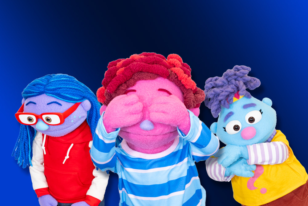 Three colorful puppet characters stand against a blue background, each with distinct hair, skin tones, and outfits expressing different emotions.