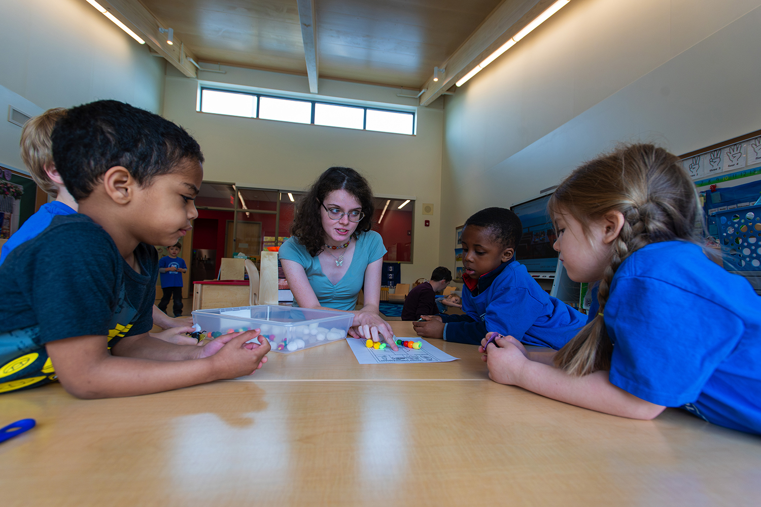 Student teacher works with elementary students at a school table.