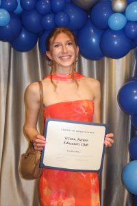 Hannah Spinner, wearing orange dress, holds award.