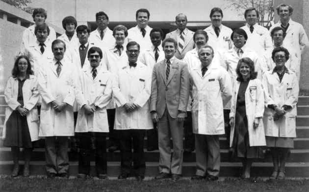 old portrait black and white three rows of people on courtyard steps, mostly wearing lab coats
