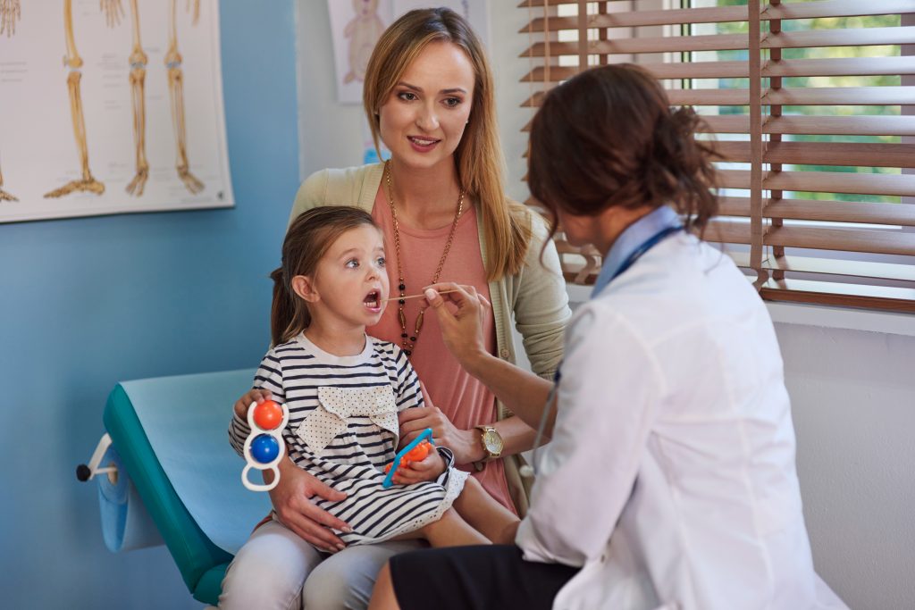 A mother and daughter in a doctor's office with the doctor looking into the child's mouth