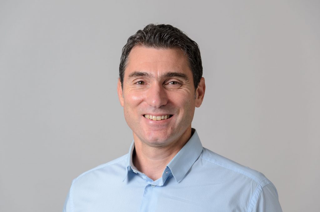 Professional headshot of a man in a blue collared shirt