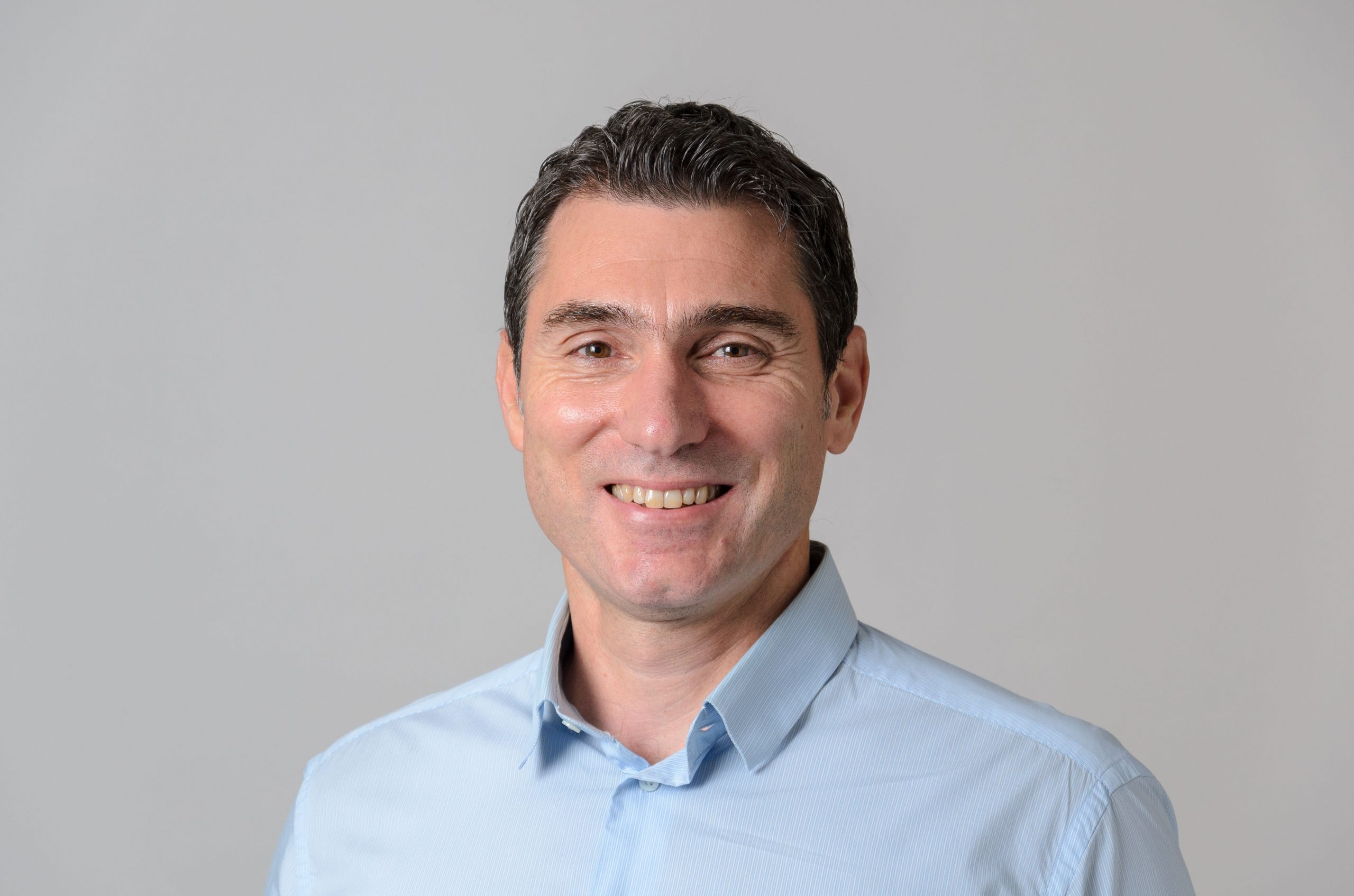 Professional headshot of a man in a blue collared shirt