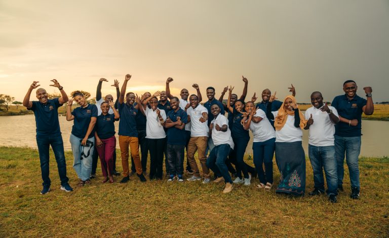 A group of excited students pose as the sun sets on the Serengeti in the background.