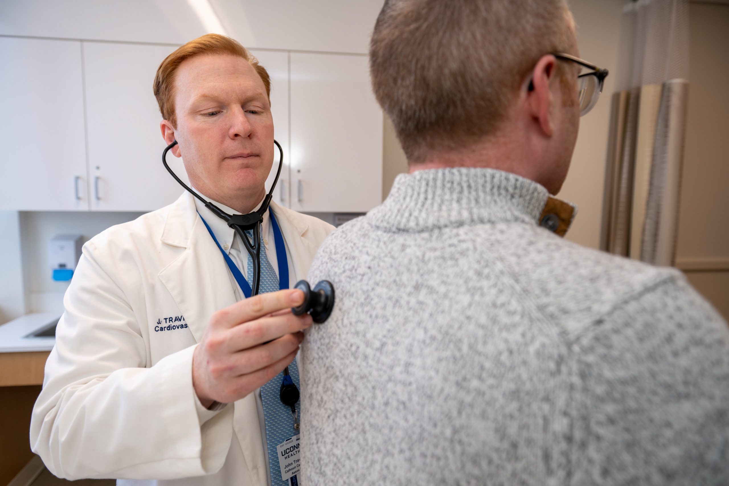 Doctor in a white coat listens to a stethoscope placed on the back of a patient
