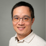 Portrait of a man wearing glasses and a light-colored polo shirt, smiling against a plain background.