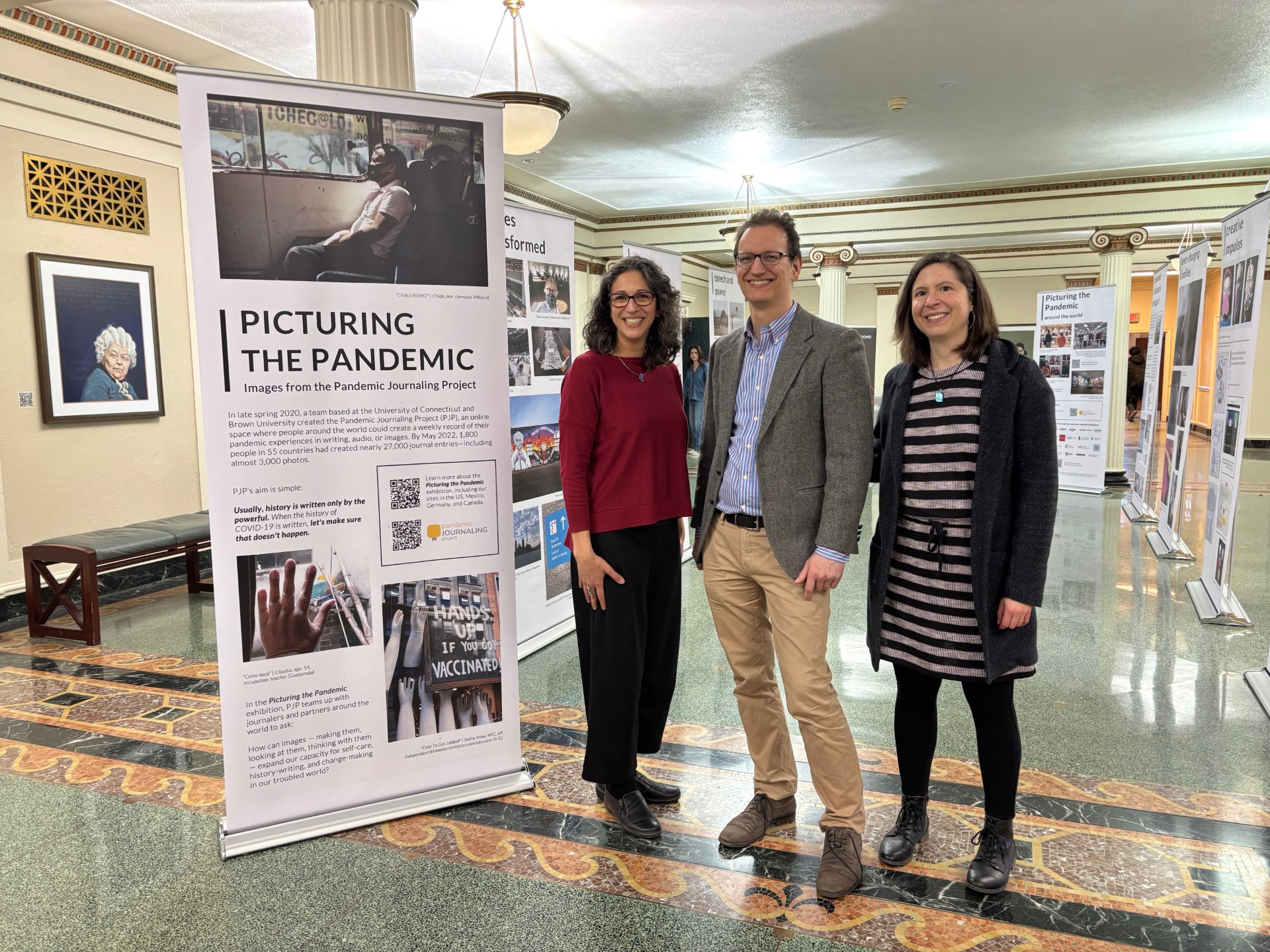 Three people standing next to a large display devoted to the Pandemic Journaling Project.