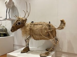 An abstract reindeer puppet is made from bent wooden reeds, burlap, and raffia.