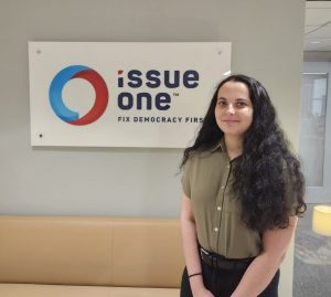 Rebecca Dorsey ’25 (CLAS), MPA ’26 stands in front of Issue One sign.