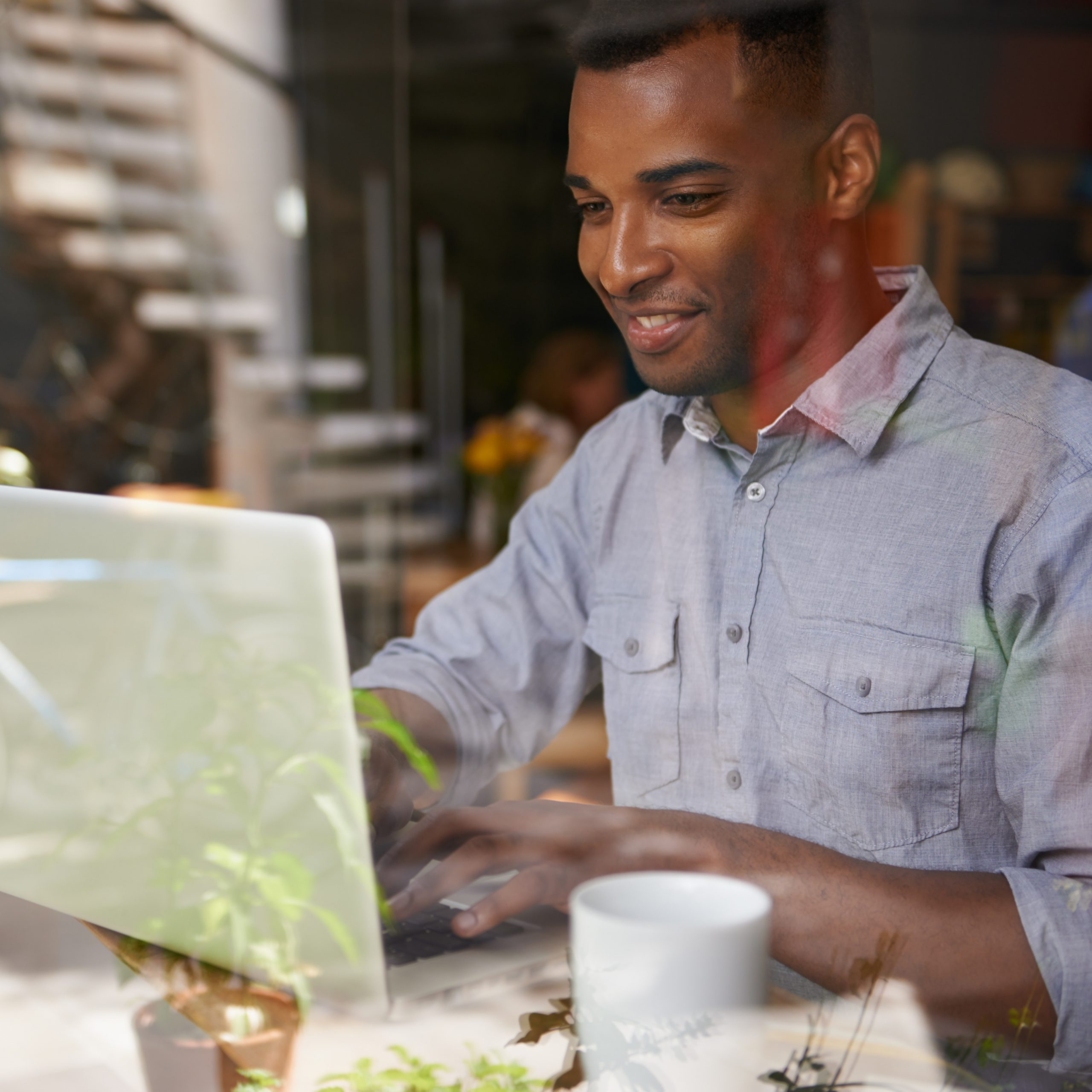 Person smiling while typing on a laptop in a bright café.