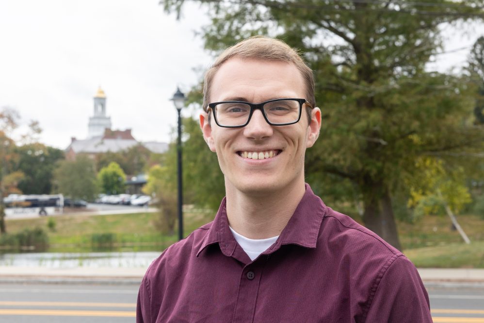 A man in glasses and a red shirt poses for a photo near Wilbur Cross