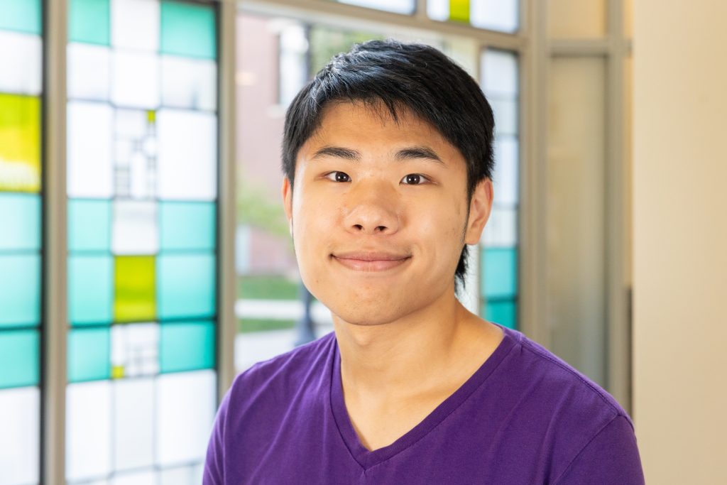 A student in front of a colorful stained glass geometric window