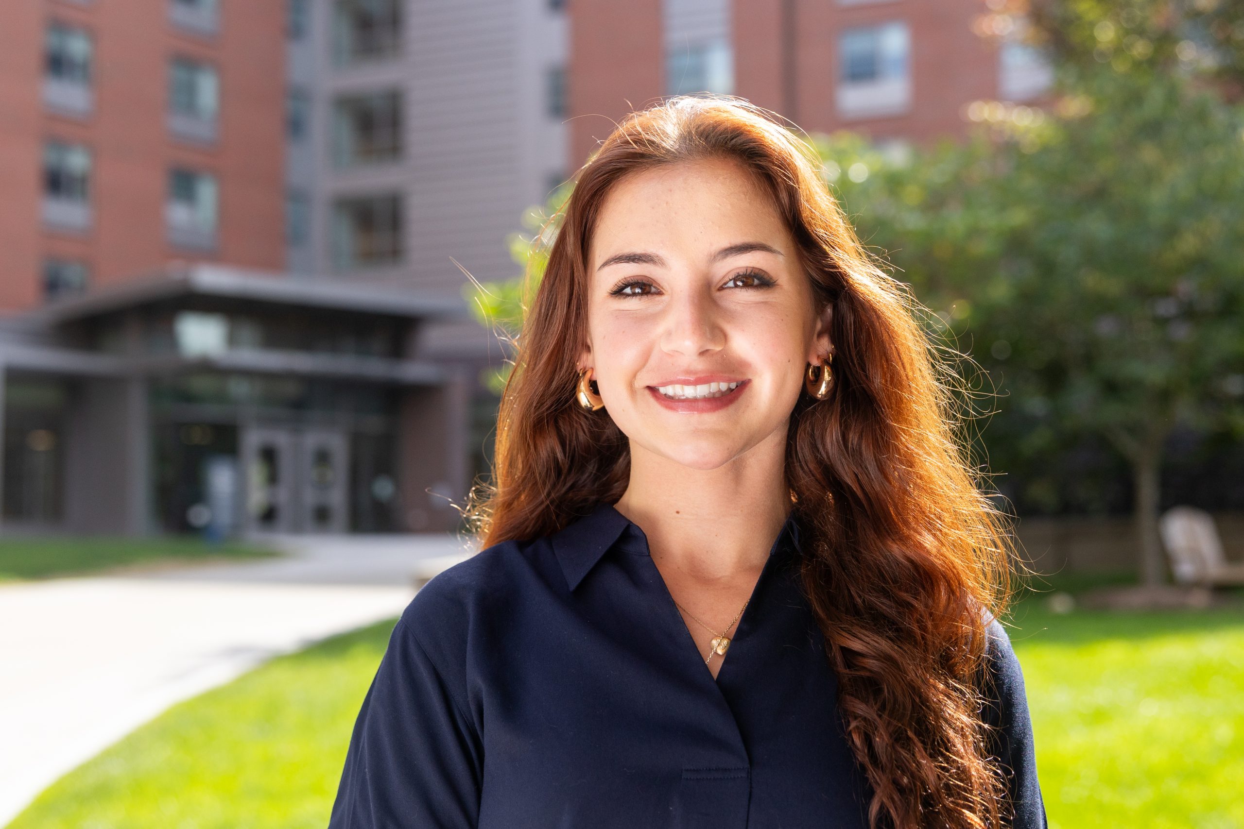 A student posing for a photo in the sunlight outside a UConn building