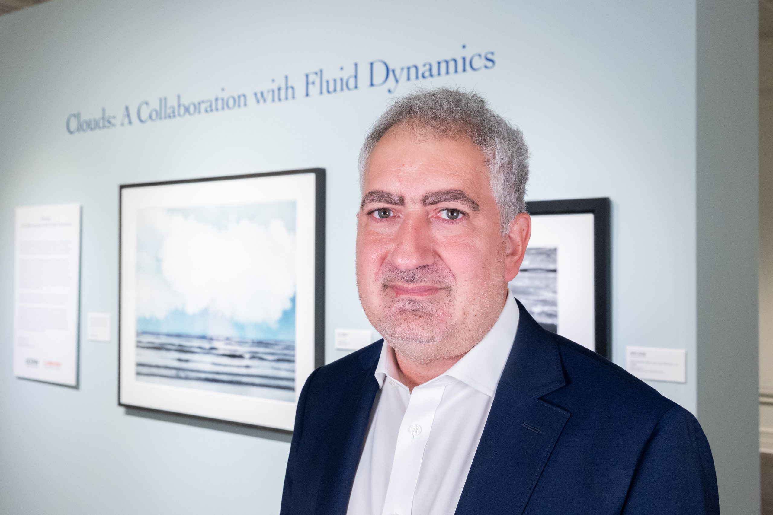 A man in a suit standing in front of a wall with cloud photos hanging