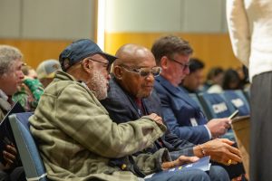 Olympians John Carlos and Tommie Smith sit together in the audience at an event.