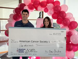 Man and women hold a big check in front of a pink balloon arch.