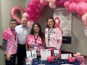 2 men and 2 women stand behind a table infront of pink balloons