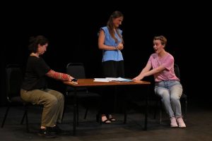 Two people sitting and one person standing around a table