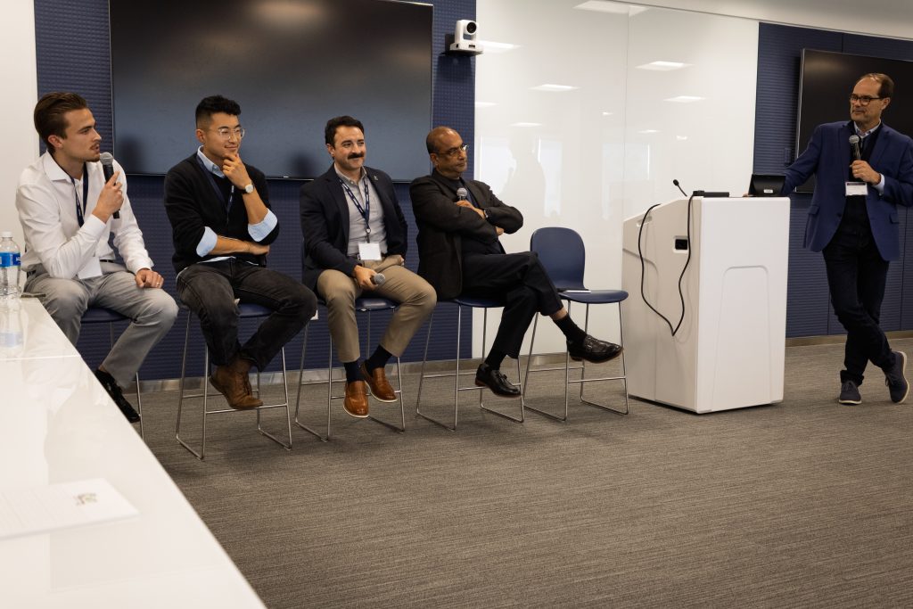 Four men engaging in a panel discussion with a moderator