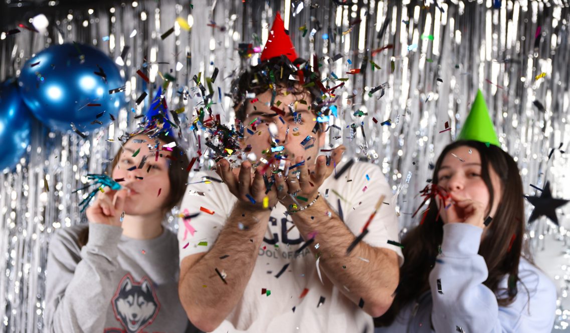 a man and two women wearing party hats and tossing confetti