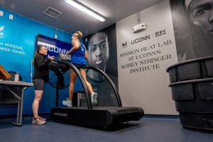 Woman runs on a treadmill in UConn's MISSION Heat Lab while researcher evaluates biometrics