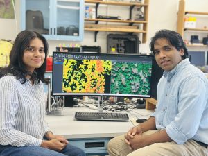 Two researchers pose before a computer screen where they are analyzing data.