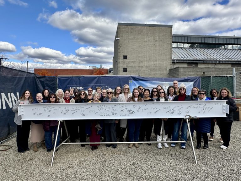 UConn Nursing faculty and staff standing behind the signed beam for the new Elisabeth DeLuca School of Nursing building.
