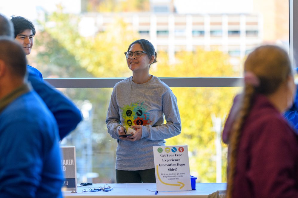 A student standing at a table talking to students walking by