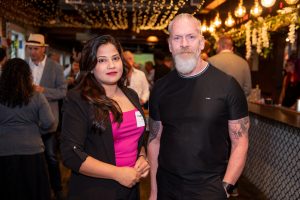A woman with dark hair and a man with a beard stand side by side, posing for a photographer.
