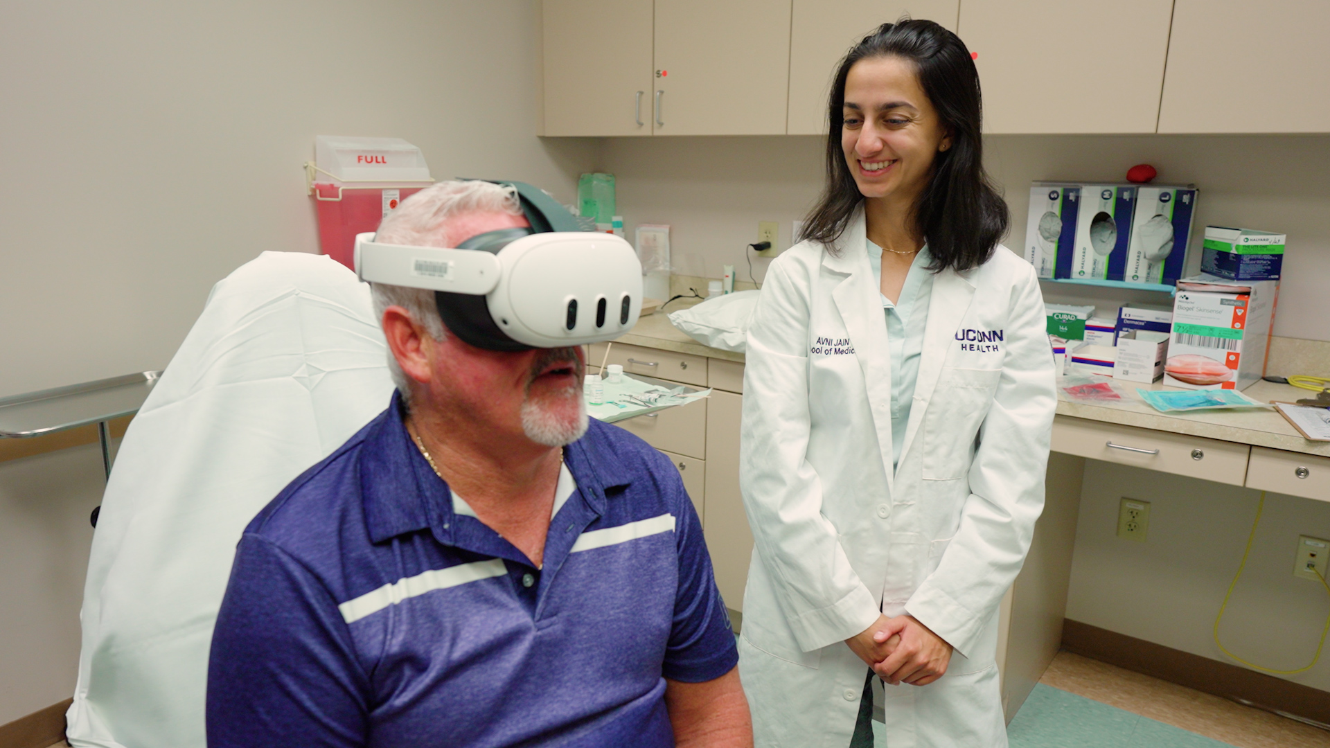 Fourth-year UConn medical student Avni Jain assists a dermatology patient with a virtual reality headset before his procedure. (Ryan Bernat/UConn Health)