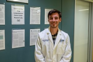 Joseph Dempsey is a research assistant stands in front of the lab at the Carole and Ray Neag Comprehensive Cancer Center at 